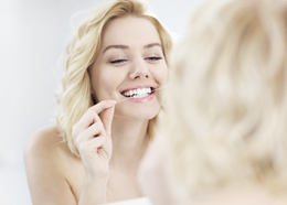 A picture of a young happy woman using dental floss in the bathroom