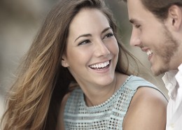 Funny couple laughing with a white perfect smile and looking each other outdoors with unfocused background